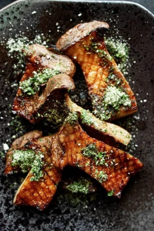 Overhead shot of cooked king oyster mushrooms drizzled with green sauce, presented on a dark plate, creating an appetizing culinary still life.