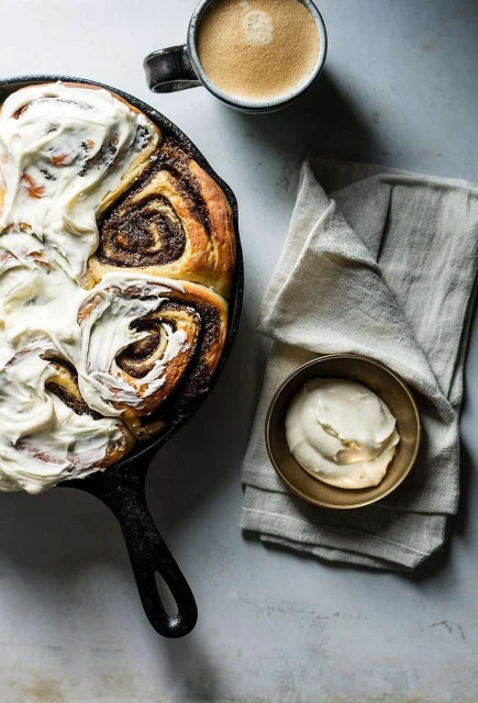 Overhead shot of cinnamon rolls with icing in a cast iron skillet next to a mug of coffee and a bowl of icing.