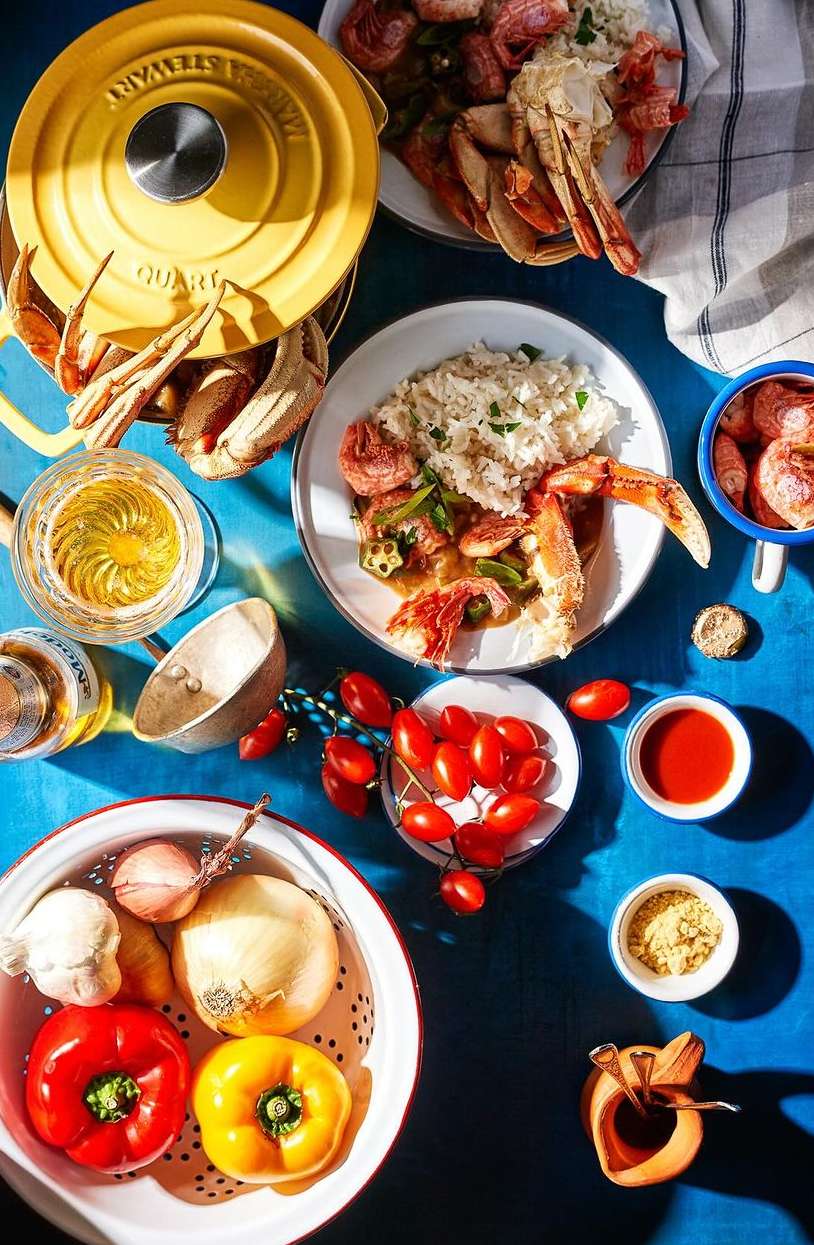 Overhead shot of a table with seafood, rice, vegetables, and various culinary ingredients arranged on a bright blue surface.