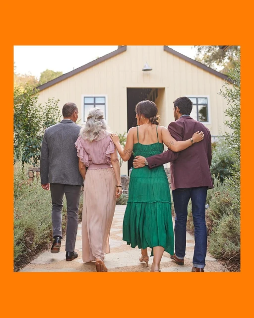 Four people walk toward a yellow building with a dark roof. Two women are linked at the arms and a couple walks behind them.