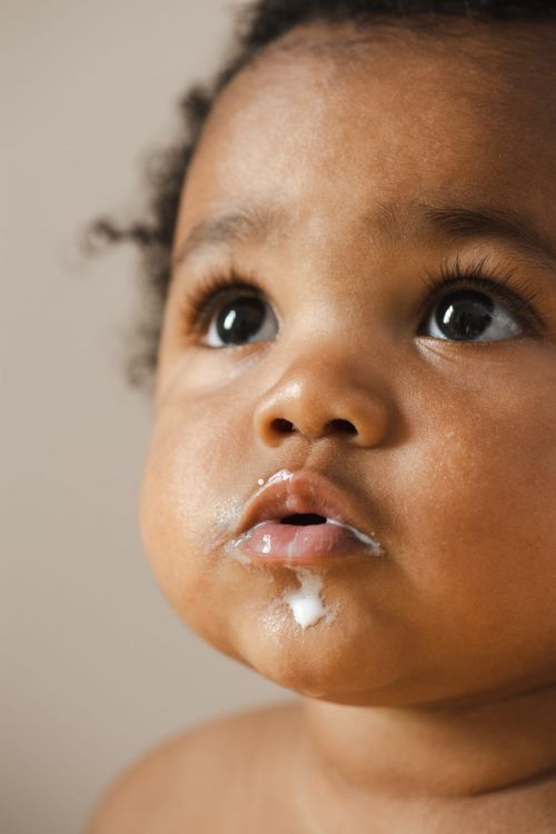 Close-up portrait of an adorable African-descent baby with dark eyes looking up, a small amount of milk or formula drooling down.
