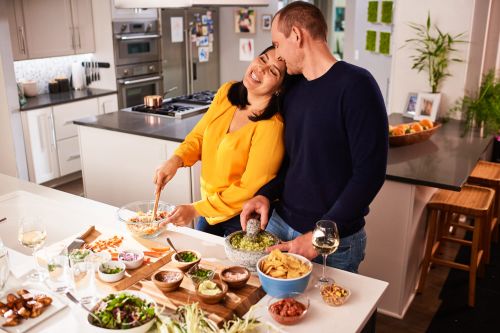 A joyful couple prepares a meal together in their home kitchen, featuring fresh ingredients and a bright, inviting atmosphere.