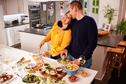 A joyful couple prepares a meal together in their home kitchen, featuring fresh ingredients and a bright, inviting atmosphere.