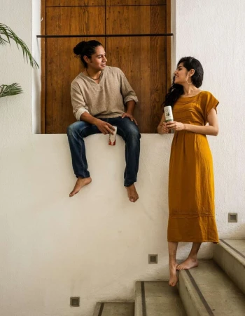 Barefoot man and woman in casual clothes hold containers indoors on stairs near a wood door and houseplants in natural light.