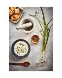 Overhead view of a bowl of dip, crackers in a tray, a mortar and pestle, and fresh green spring onions.