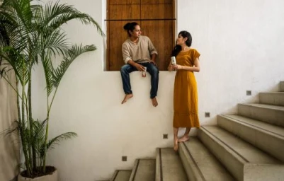 Man sitting on a wooden window ledge and woman standing on concrete stairs talking, photographed by Dawn Heumann.