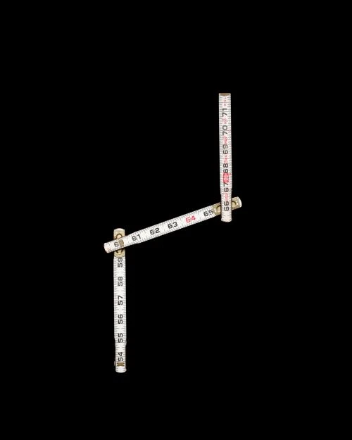 Measuring stick forming a right angle on a black background, with numbers and hash marks indicating measurements in inches or centimeters.