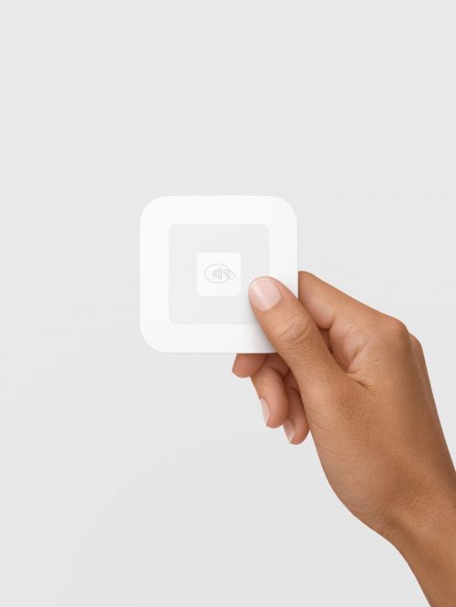 Close-up of a square, white Square card reader held in a person's hand against a neutral background.
