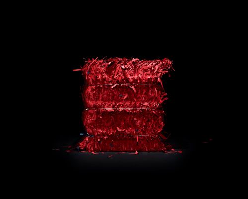 A stack of translucent red paper or plastic shavings tied with wire, illuminated in a dark space against a black background.