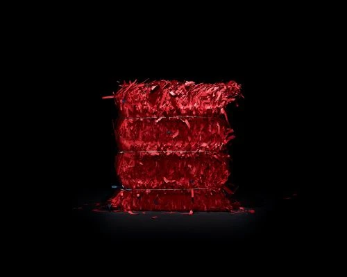 A stack of translucent red paper or plastic shavings tied with wire, illuminated in a dark space against a black background.