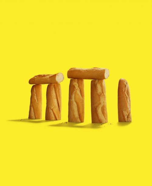 Stonehenge made of bread baguettes on a bright yellow background, creating a whimsical and surreal food composition.