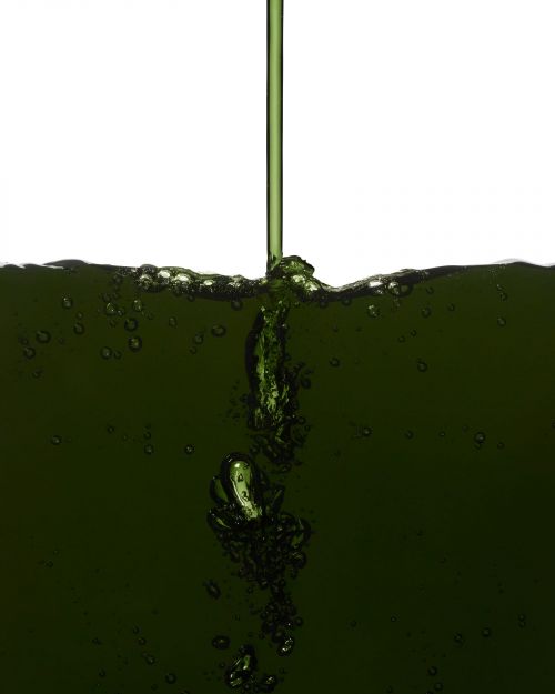 Pouring of green liquid with bubbles into a clear container against a white background, showcasing liquid dynamics and simple composition.