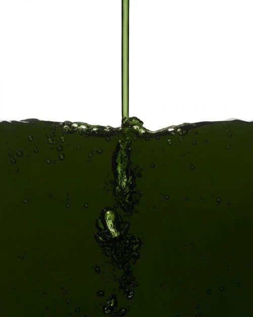 Pouring of green liquid with bubbles into a clear container against a white background, showcasing liquid dynamics and simple composition.