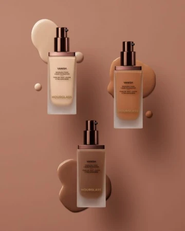 Three bottles of Hourglass Vanish foundation in different shades arranged with matching foundation smears on a neutral background.