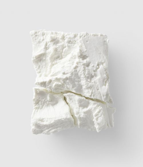 Close-up overhead shot of a block of white feta cheese with visible cracks, set against a plain light grey background, food photography.