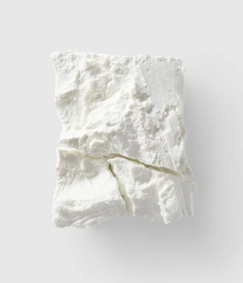 Close-up overhead shot of a block of white feta cheese with visible cracks, set against a plain light grey background, food photography.