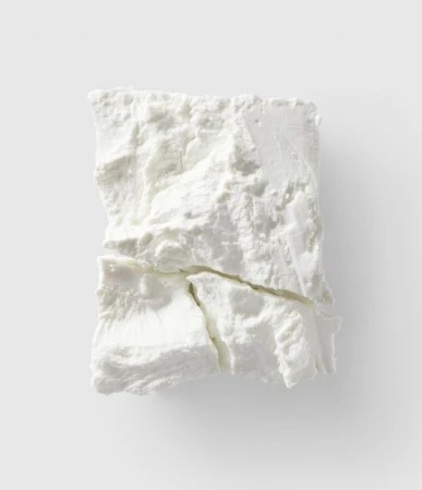 Close-up overhead shot of a block of white feta cheese with visible cracks, set against a plain light grey background, food photography.