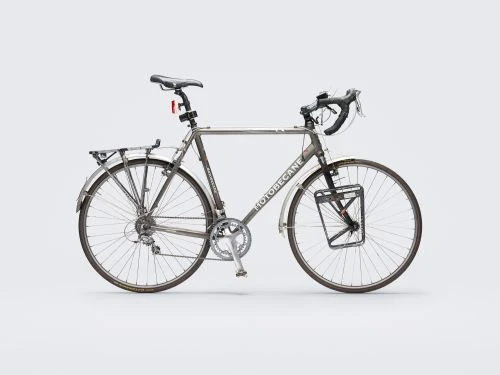Silver Motobecane bicycle with accessories, including a rear rack, fenders, and front carrier, standing against a neutral gray background.