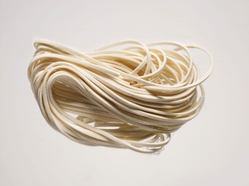 Close-up studio shot of a tangled bundle of fresh, uncooked, thick white noodles against a plain, light background creating a simple food still life.