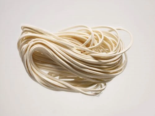 Close-up studio shot of a tangled bundle of fresh, uncooked, thick white noodles against a plain, light background creating a simple food still life.