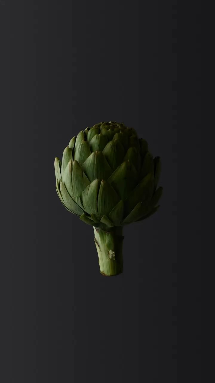 Close-up still life shot of a green artichoke on a dark background with a smooth texture and dramatic lighting.
