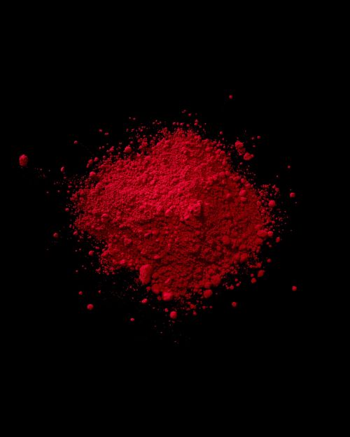 Vibrant heap of red powder pigment on a stark black background, creating a striking contrast in colour and texture, studio shot.