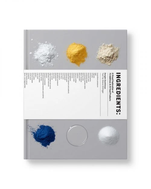 Close-up still life photo of a book cover with piles of colorful powder, presented against a clean white backdrop. 