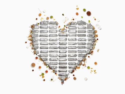 Overhead shot of candy bars arranged in a heart shape with colorful sprinkles and crumbs on a white background, creating a sweet and festive composition.