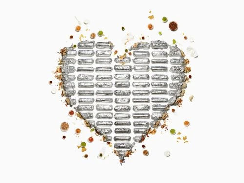 Overhead shot of candy bars arranged in a heart shape with colorful sprinkles and crumbs on a white background, creating a sweet and festive composition.