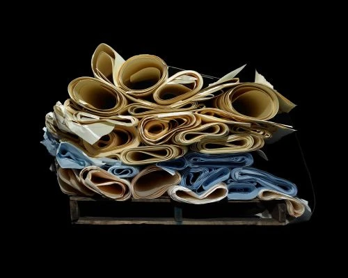 Stack of rolled blueprints in tan and blue hues resting on a wooden pallet, set against a stark black background.