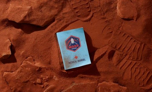 Medical manual on a red surface resembling Mars, featuring red rocks and subtle footprints, with the cover partially obscured.