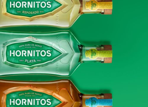 Three Hornitos tequila bottles sit on a green background. The bottles are Plata, Reposado, and Anejo. Each bottle has a label and wooden cap.