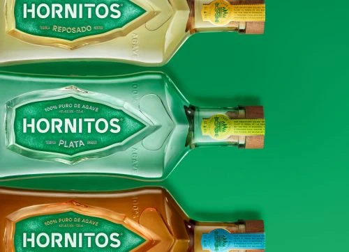Three Hornitos tequila bottles sit on a green background. The bottles are Plata, Reposado, and Anejo. Each bottle has a label and wooden cap.