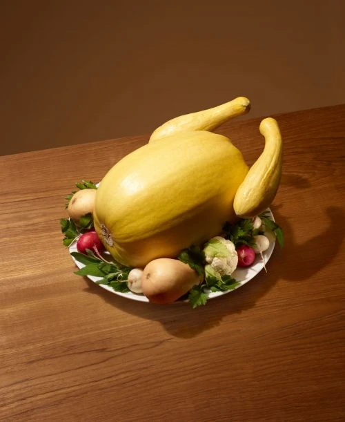 Still life of yellow spaghetti squash crafted into a turkey shape surrounded by radishes, cauliflower and parsley on wooden table.