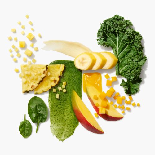 Overhead food photo of fruit and green vegetables including pineapple, mango, banana, kale, and spinach on a white surface.