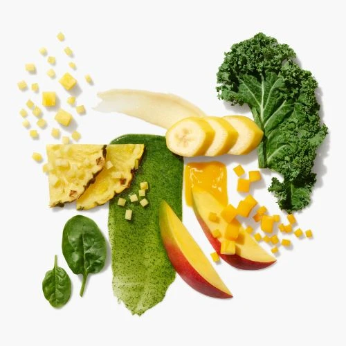 Overhead food photo of fruit and green vegetables including pineapple, mango, banana, kale, and spinach on a white surface.