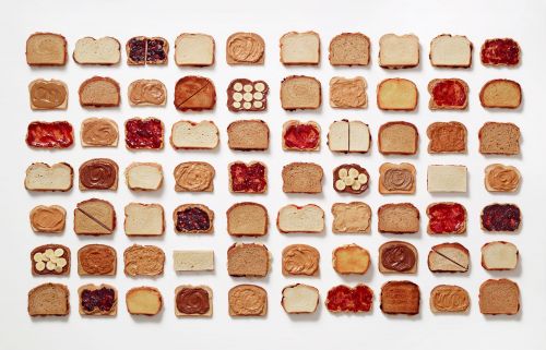 Overhead flat lay of 56 slices of toasted bread, each with different toppings like peanut butter, jelly, banana, and chocolate.