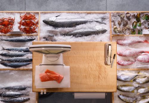 Overhead shot of a market display featuring an assortment of fresh seafood, including whole fish, crabs, and salmon fillets on ice.