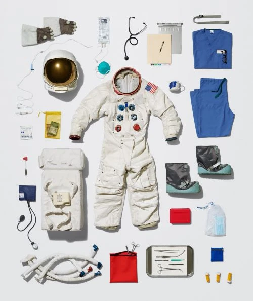 Overhead shot of an astronaut spacesuit surrounded by various medical supplies on a bright white background in a flat lay composition.
