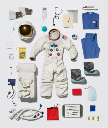 Overhead shot of an astronaut spacesuit surrounded by various medical supplies on a bright white background in a flat lay composition.