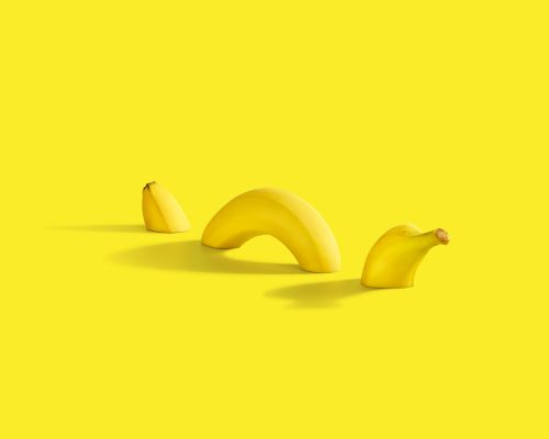 Creative still life with three banana pieces on a yellow background, creating an abstract and minimalist composition.