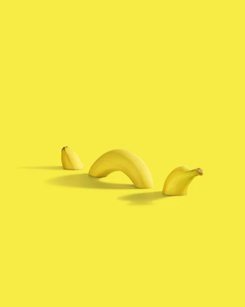 Still life photograph of three banana peels of varying sizes arranged on a bright yellow background, casting soft shadows.