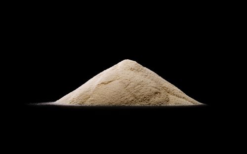 A pile of white powder sits in the center of a black background, casting a slight shadow and creating a minimalistic food still life.