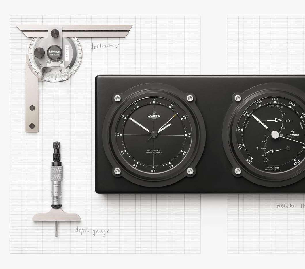 Close-up of black-faced Wempe Navigator instrument panel with clock, barometer, depth gauge, protractor, and graph paper backdrop.