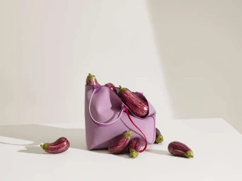 Purple tote bag filled with striped eggplants resting on a white surface with loose eggplants scattered around