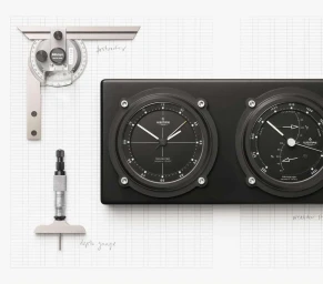 Top-down view of black nautical instruments and silver precision measuring tools arranged on a white grid paper background.