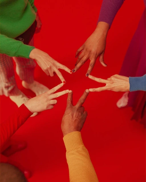 Group of diverse hands creating a star shape against a vibrant red background, showcasing unity and teamwork with brightly coloured sleeves.