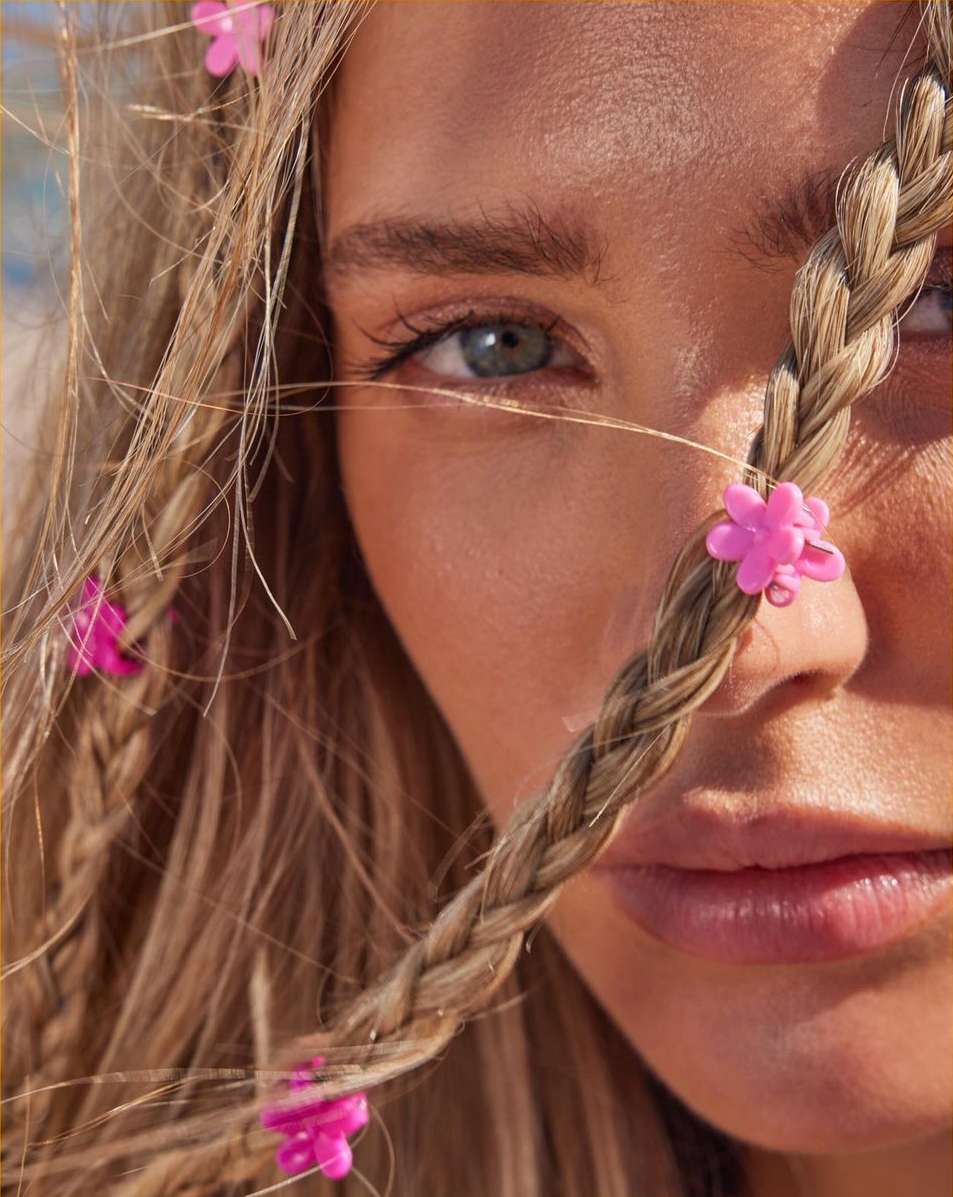 Close-up portrait of a young fair-skinned woman with blond braided hair adorned with pink flower clips, capturing her serene expression.