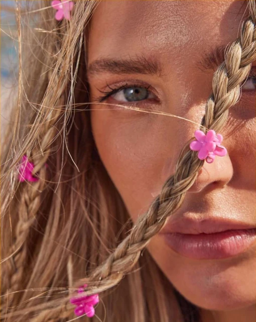 Close-up portrait of a young fair-skinned woman with blond braided hair adorned with pink flower clips, capturing her serene expression.