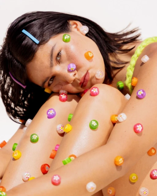 Brunette woman with hair clips and decorative flower beads covering her face and body posing against a white studio backdrop.